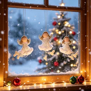 Drie handgemaakte fonkelende kerstengeltjes die voor een gezellig besneeuwd raam hangen.