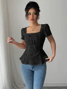 Vista detallada de una elegante blusa de encaje negro con escote cuadrado y detalle de lazo.