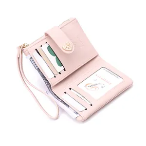 Detail view of pink short bi-fold wallet with a heart-shaped gold buckle and wrist strap.