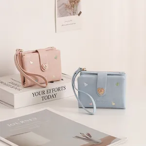 Close-up detail of heart-embroidered short fold wallets in pastel pink and soft blue colors