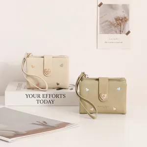 Two stylish heart-embroidered wallets in cream and sage green displayed on minimalist props
