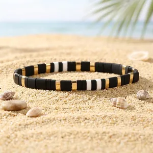Detailed view of bohemian black white and gold enamel tile stretch bracelet on beach sand