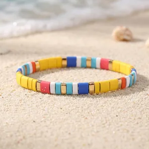 Detailed view of a vibrant colorful enamel tile stretch bracelet resting on a sunny sandy beach