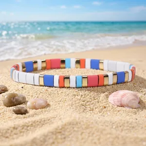 Detail view of a colorful enamel tile stretch bracelet on a sunny beach sand background.