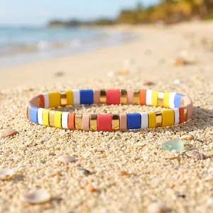 Detailed view of colorful enamel tile stretch bracelet resting on sunny beach sand