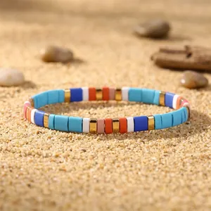 Close-up of a colorful enamel tile stretch bracelet placed on natural beach sand