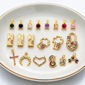 A collection of gold-plated charms featuring colorful zircon settings on a white ceramic plate