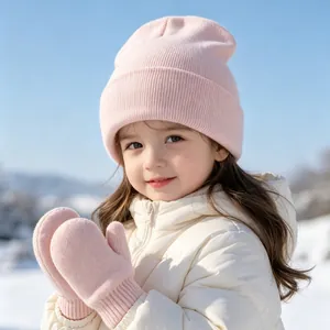 Adorable toddler wearing a pink knit winter hat and mittens set in a snowy scene