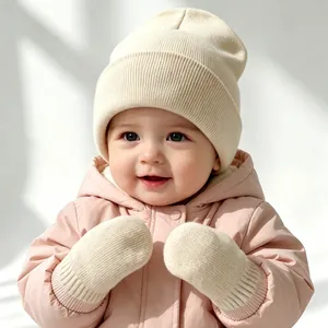 Detailed view of a cute infant wearing a cream knit beanie and matching mittens set