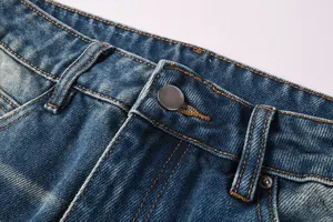 Detailed macro view of mens blue denim flared jeans showing waist button and yellow stitching
