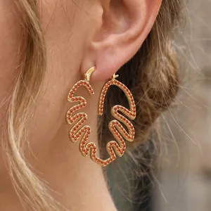 Nahaufnahme des vergoldeten Monstera-Blatt-Ohrrings mit orangen Zirkonia-Steinen.