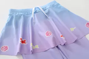 Detailaufnahme eines Mädchen-Schwimmrocks mit blau-violettem Farbverlauf und Meeresmotiven