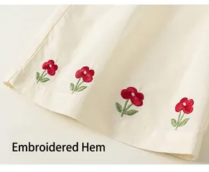 Dettaglio del ricamo a fiori rossi sulla gamba dei pantaloni da bambina color crema
