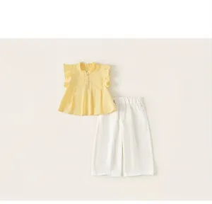 Dettaglio di un set estivo per bambine con top giallo a balze e pantaloni bianchi