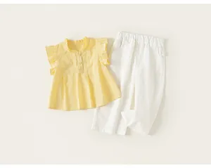 Dettaglio dell'completo estivo per bambina: top giallo a balze e pantaloni bianchi