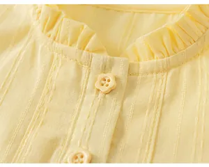 Dettaglio di un top senza maniche giallo per bambina con colletto a balze e bottone floreale