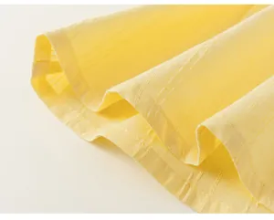 Dettaglio ravvicinato della trama a pieghe e dell'orlo cucito del top giallo da bambina