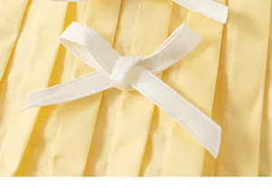 Dettaglio macro ravvicinato di un fiocco bianco su top a pieghe giallo per bambina
