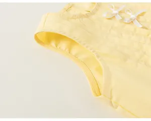 Dettaglio di un top giallo senza maniche plissettato per bambine con fiocchi bianchi