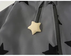 Detail of children's grey windbreaker featuring black star patterns and yellow star zipper pull