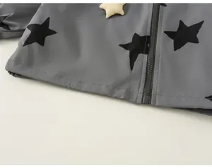 Macro detail view of child's grey windbreaker with black star print and zipper.
