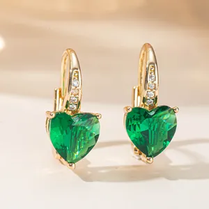 Close-up of elegant gold earrings with heart-shaped green gemstones and cubic zirconia