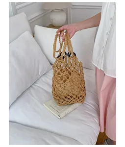 Hand-held view of a beige hollow out woven macrame bag in a lifestyle setting