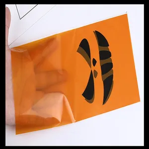 Detail view of an orange Halloween pumpkin face plastic treat bag held by a hand.