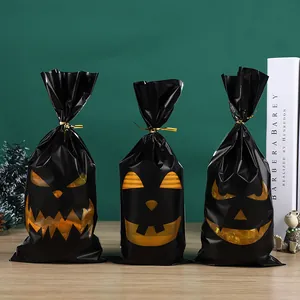 Three black Halloween pumpkin face candy bags with gold twist ties on green background