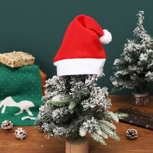Rote Plüsch-Weihnachtsmütze für Erwachsene auf kleinem Tannenbaum für Festdekoration.