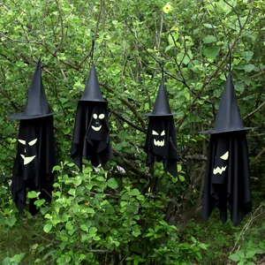 Four hanging Halloween witch hat ghost decorations with glowing faces against lush green bushes.