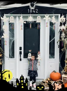 Κοριτσάκι κρατά ξύλινη DIY κατασκευή για το Halloween μπροστά από στολισμένο σπίτι