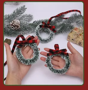 Hands holding mini frosted Christmas wreaths with red and black buffalo plaid bows.