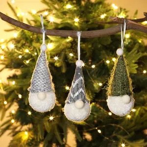 Three handcrafted knitted Christmas gnome ornaments hanging on a branch with warm lights