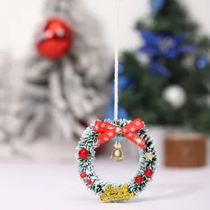 Mini corona de Navidad verde nevada con un lazo rojo y un pequeño cascabel dorado colgante
