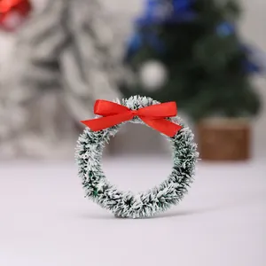 Mini kerstkrans met sneeuweffect en rode strik voor feestelijke tafeldecoratie.
