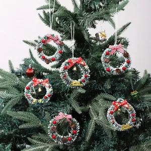 Mini coronas de Navidad nevadas con piñas, bayas y lazos rojos en un árbol