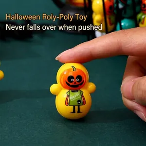 Mini Halloween pumpkin tumbler toy for kids, shown being pressed by a finger on green background