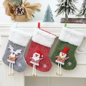 Set of three plush Christmas stockings with hanging legs and bells for fireplace decoration.
