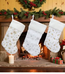 Dettaglio di tre calze di Natale in peluche bianco con fiocchi di neve dorati vicino al camino
