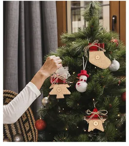 Nahaufnahme einer Hand, die rustikalen Jute-Weihnachtsschmuck an einen Tannenbaum hängt.