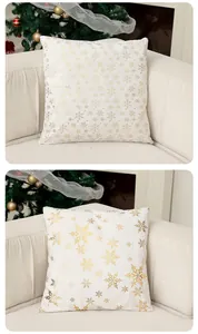 Vue détaillée de housses de coussin de Noël blanches avec flocons dorés sur un canapé douillet.