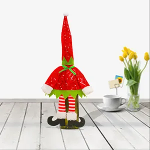 Feestelijke kerstelf wijnfleshoes met rode muts en gestreepte benen voor tafeldecoratie.