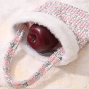 Pink and silver knitted Christmas gift bag with white fur trim and a red apple inside.