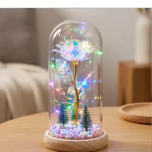 Rosa de cristal luminosa en cúpula de vidrio con luces LED y pequeños pinos de Navidad.