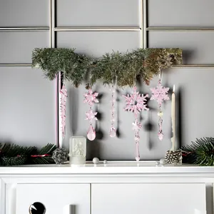 Adornos de copos de nieve y carámbanos de acrílico rosa colgados en una guirnalda de pino.