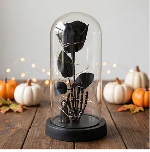 Detalle de rosa negra de Halloween en cúpula de cristal sostenida por mano de esqueleto