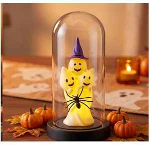 Detail of glowing Halloween ghost figurines in a glass dome with a spider accent
