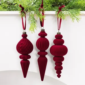 Detaillierte Nahaufnahme roter Samt-Weihnachtsornamente, die an grünen Zweigen hängen