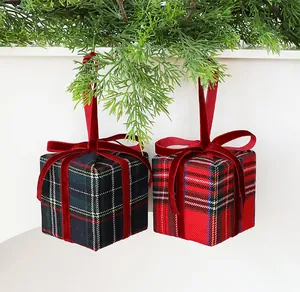 Primo piano di due addobbi natalizi a forma di scatola regalo con fiocchi di velluto rosso.